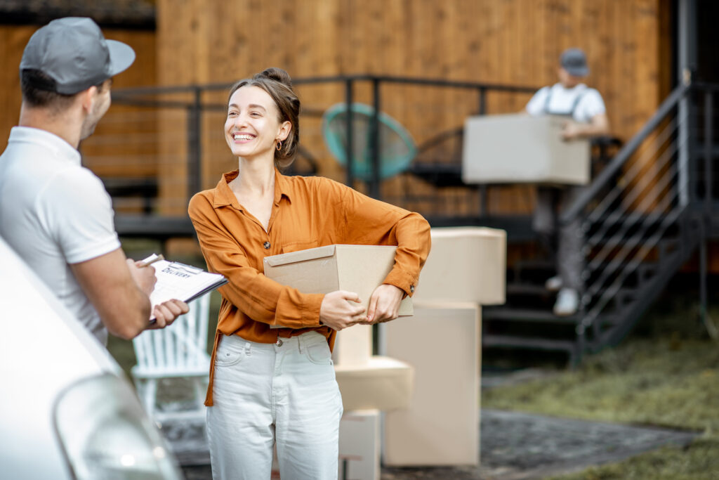 Portrait of a happy client with a male courier delivering goods by vehicle to a woman home, workman moving parcels on the background