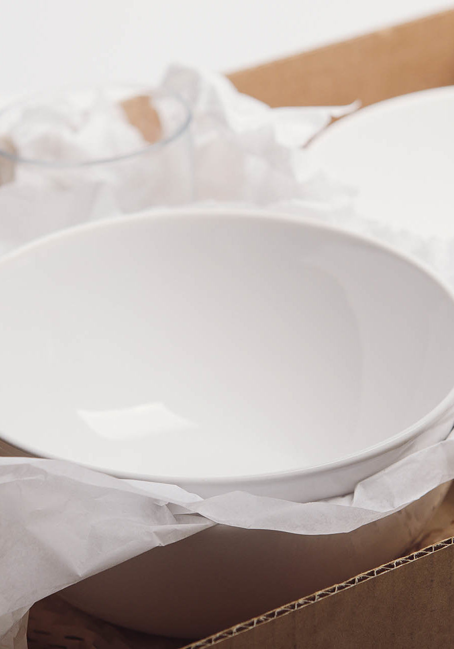 Clean white dishes in paper packed in cardboard box. Concept relocation.